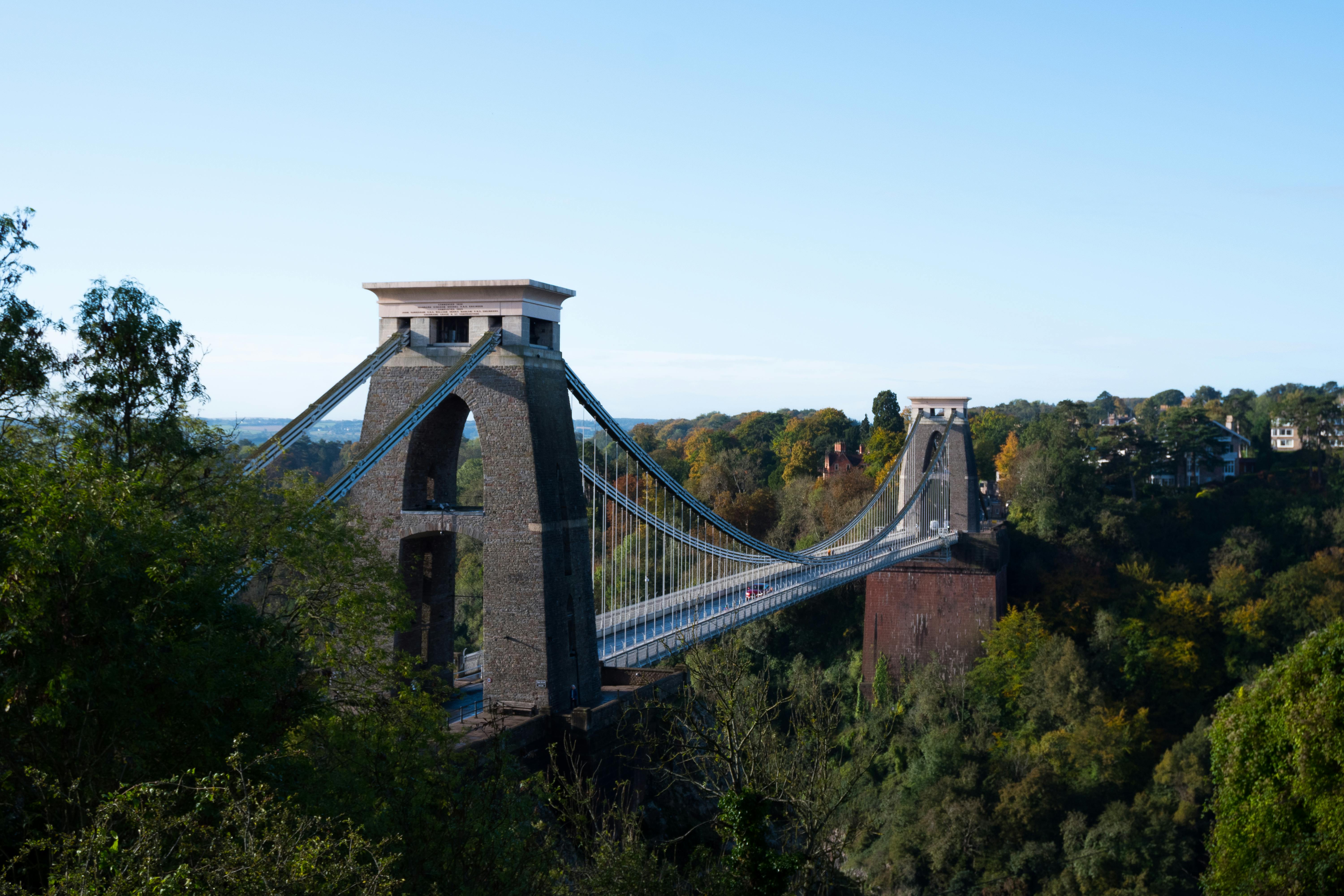 Clifton Suspension Bridge in Bristol, viewed from the side with trees and Avon Gorge below — symbol of Bristol's enduring engineering and community heritage